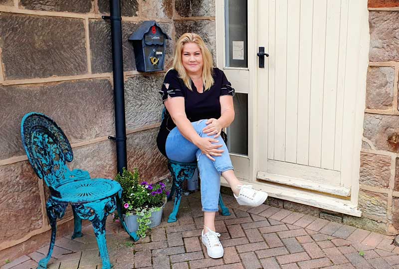 Susie sitting on a chair in front of her house which is a barn conversion and no dangerous metal in sight